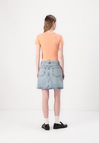 Maglietta crop arancione abbinata a una gonna in denim azzurro chiaro con un motivo logo discreto. Scarpe nere e calzini bianchi completano il look.