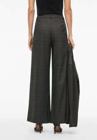 Sive karirane široke hlače s narančastim akcentima, krojene prilagodbe, visokog struka i glatke teksture tkanine. Model drži odgovarajući sako.