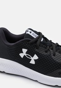 Scarpa sportiva nera con tomaia in rete testurizzata, dettagli bianchi e suola ammortizzata. I lacci sono neri, con un logo sulla linguetta.