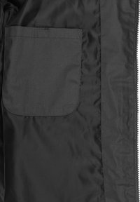 Intérieur de veste en tissu noir et lisse avec une poche rectangulaire cousue sur le côté gauche. Fermeture éclair sur le bord droit.