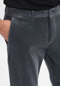 Spodnie sztruksowe w ciemnoszarym kolorze z pionowymi prążkami, przednią kieszenią i zapięciem na guzik; cechują się gładką teksturą i dopasowanym krojem.