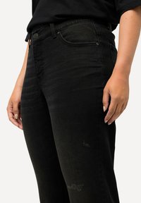Vaqueros de mezclilla negra con un diseño ajustado, un ligero estiramiento y sutiles detalles desgastados en la parte frontal. Estilo clásico de cinco bolsillos.