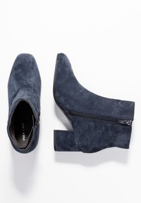 Botines de ante azul marino con un tacón grueso, que cuentan con un cierre lateral y un diseño de punta afilada. Textura suave y estilo minimalista.