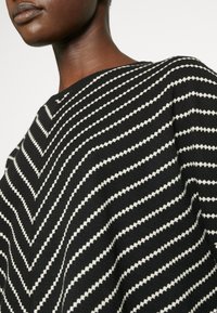 Black and white striped knit top featuring a chevron pattern, with a textured fabric. Close-up view emphasizing the pattern's detail.
