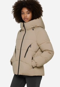 Giacca puffer beige con colletto alto, zip frontale e zip nere in contrasto. Presenta un cappuccio oversized e una texture trapuntata per l'isolamento.