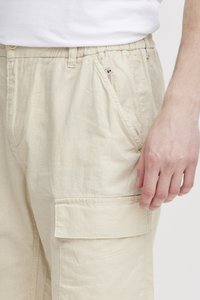 Pantalons cargo en lin beige avec une taille élastique, des poches latérales et une poche à rabat sur la cuisse. Texture lisse et tissu léger.