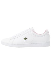 Sneaker bianche con bordino rosa, dotate di un piccolo logo di coccodrillo verde vicino ai lacci e tre fori di ventilazione sul lato esterno.