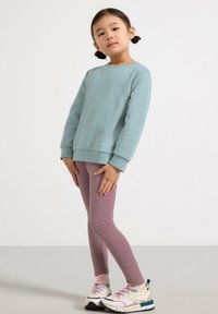 Lyseblå sweatshirt med rund hals, kombineret med pink leggings og multikolore sneakers med en marmorert sål. Glat struktur.