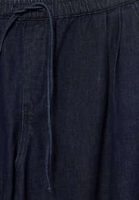 Țesătură denim indigo închis cu cusături vizibile și șnur legat în talie, evidențiind textura și pliurile.