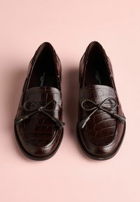 Mocasini maro cu embosare tip piele de crocodil, cu partea superioară din piele netedă. Prezintă o fundă decorativă și ciucuri în față. Design texturat și elegant.