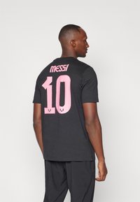  camiseta negra de algodón con un gráfico rosa de "10" y "MESSI" en la parte posterior, con cuello redondo y mangas cortas. Diseño minimalista.