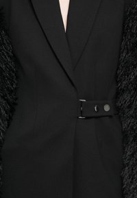 Black blazer with textured fur-like sleeves, featuring a fitted silhouette, notched lapels, and a side belt with two buttons.
