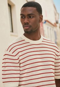 Strikket sweater med en cremefarvet bund og røde horisontale striber, korte ærmer og rund halsudskæring. Teksturomateriale i let vægt.