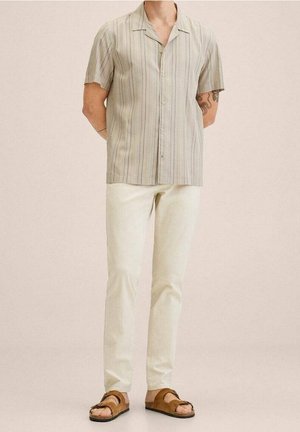 Korte mouwen, knoopsluiting shirt in lichtbeige met dunne verticale strepen, gecombineerd met crèmekleurige broek en bruine sandaal.