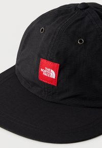 Μαύρο καπέλο με ευρύ γείσο, με κόκκινο τετράγωνο έμπλαστρο που εμφανίζει το λογότυπο "THE NORTH FACE". Μεταλλικά ρουμπάκια για αερισμό. Λεία υφή.