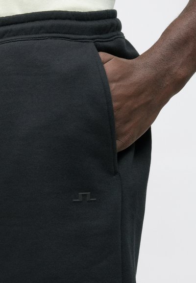 Pantalon de survêtement noir avec une texture douce, une taille élastique, une poche latérale avec un discret accent logo.