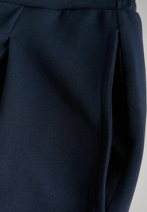 Mörkblå joggingbyxor tillverkade av mjukt, elastiskt tyg med sidofickor och veckdetaljer. Slät textur och avslappnad design.