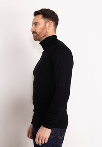 Maglione a collo alto nero con design aderente, realizzato in un materiale a maglia liscia, abbinato a jeans in denim scuri, dotati di finiture semplici per i polsini e l'orlo.
