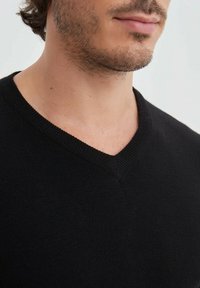 Pull noir à col en V avec un col côtelé, fabriqué dans un matériau doux et texturé ; design ajusté mettant en valeur l'encolure.