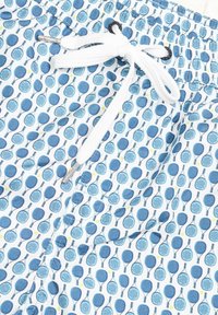 Costumi da bagno in tessuto bianco con motivo a racchette blu e dettagli gialli. Presentano una vita elastica con lacci bianchi.