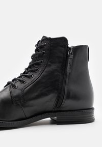 Černá kotníková botka z kůže se šněrováním vpředu a bočním zipem, kulatou špičkou a texturovanou podrážkou. Hladký povrch s minimálním zdobením.