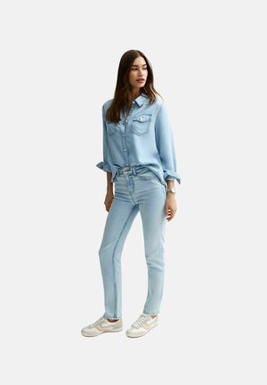 Lichtblauwe denim shirt met twee borstzakken, gecombineerd met lichtblauwe jeans en beige sneakers. Het shirt heeft opgerolde mouwen en eenvoudige stiksel.