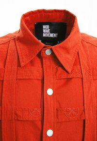 Camisa roja de botones con un collar estructurado, dos bolsillos en el pecho, botones plateados y adornos de costura decorativos.