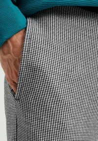 Šedý a bílý kostkovaný vzor látky s hladkým texturem; viditelná kapsa s tyrkysovým žebrovaným detailem nahoře.