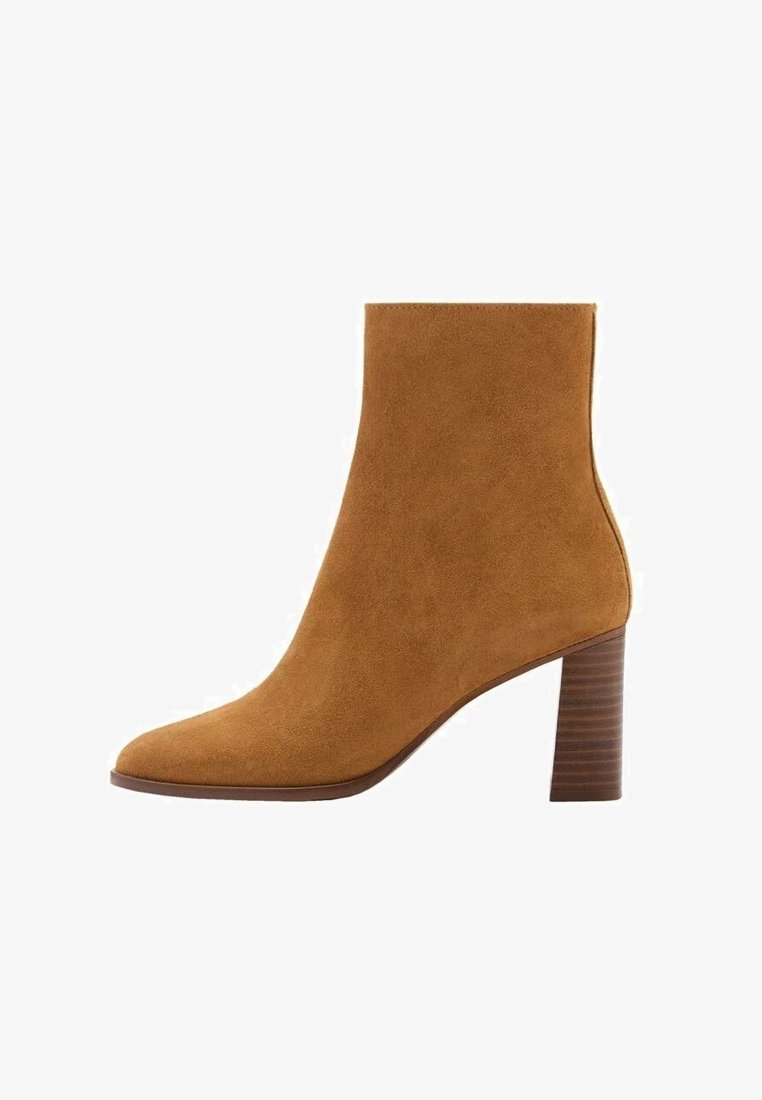 Bottine en daim beige, dotée d'un bout pointu et d'un talon bloc empilé. Sa texture lisse et ses lignes épurées forment une silhouette moderne.