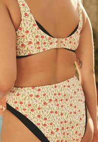 Swimsuit featuring a floral pattern with red cherries and small white flowers on a green background, accented with black fabric trim.
