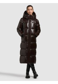 Pikk, läikiv pruun sulejope kapuutsiga, millel on horisontaalne triibutus ja tõmblukuga taskud. Kandmisel mustade põlveni ulatuvate saapade peal.