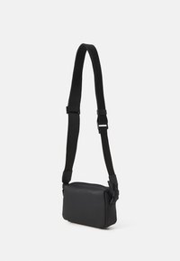Sac bandoulière noir avec une texture lisse, de forme rectangulaire, une sangle ajustable et une fermeture éclair. Design simple et minimaliste.