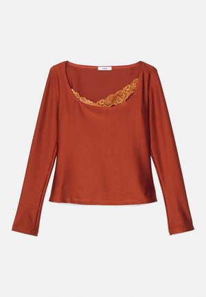 Haut à manches longues en orange rouille, avec un décolleté rond orné d'une délicate bordure en dentelle jaune, fabriqué à partir d'un matériau doux et extensible.