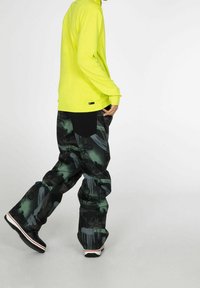Camisa de manga larga amarilla neón combinada con pantalones holgados de patrones en negro y verde oscuro, con una textura notable y gráficos visibles.