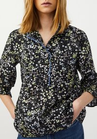 Blusa nera con un motivo floreale in verde, blu e bianco. Presenta una patta con bottoni, un colletto arricciato e maniche a tre quarti.