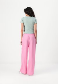 Top a maniche corte di un verde chiaro a coste con orlo scallop abbinato a pantaloni rosa a vestibilità larga realizzati in tessuto texturizzato.