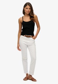 Top nero senza maniche con spalline, jeans bianchi aderenti, cintura marrone, sandali marroni. Tessuto testurizzato, design minimalista, colori neutri.
