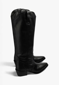 Botas de cuero negras hasta la rodilla con punta afilada, tacón apilado y detalles de costura a lo largo de los costados. Textura suave y diseño minimalista.
