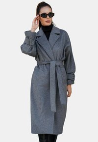 Szary płaszcz trench z wełny z domieszką, z paskiem w talii, dużym kołnierzem i zapinanymi mankietami, o luźnym kroju i minimalistycznym designie.