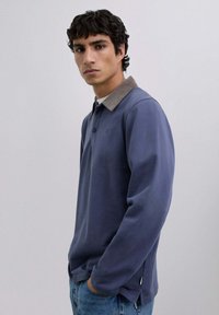 Long-sleeve polo shirt in navy, featuring a contrasting beige collar, two-button placket, and subtle logo on the chest. Soft cotton fabric.