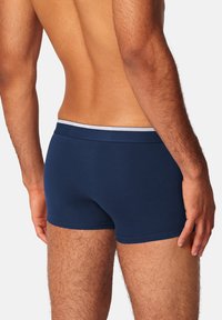 Marineblaue Boxershorts aus weichem Stoff, mit einem kontrastierenden weißen elastischen Bund und einem enganliegenden Design.