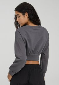 Szara, skrócona bluza z długimi rękawami i elastycznym pasem. Miękka tekstura materiału, casualowy fason i ściągacze przy mankietach. Noszona z czarnymi spodniami.