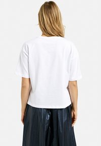 Weißes Baumwoll-T-Shirt mit Rundhalsausschnitt, kurzen Ärmeln und lockerer Passform, kombiniert mit einem glänzenden schwarzen Plissierrock.