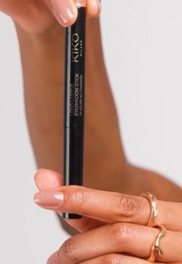 Pitkäkestoinen luomivärikynä tyylikkäässä mustassa kotelossa, jossa on sileä koostumus. Käsi, jossa on vaaleanpunainen kynsinauha, pitää tuotetta.