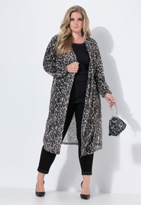 Leopardmönstrad lång kimono i genomskinligt tyg, öppen framtill, kombinerad med en svart topp och byxor. Tillbehör inkluderar en paljett-handväska.