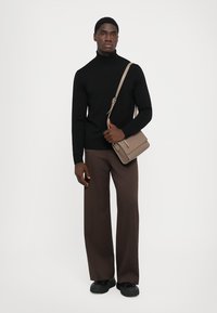 Pulover negru cu guler înalt, pantaloni largi maronii și o geantă bej de umăr, accesorizate cu pantofi negri, pe un fundal alb simplu.
