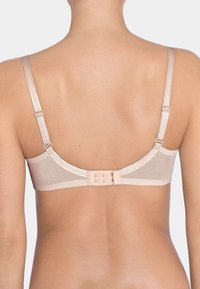 Nuden värinen rintaliivi, jossa on sileä pinta, säädettävät olkaimet ja koukku- ja silmukkasuljenta. Siinä on yksinkertainen muotoilu, jossa on vain vähän koristuksia.