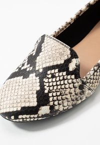 Chaussure plate pointue avec un motif en serpentin noir et beige et un design légèrement découpé près du bord supérieur.