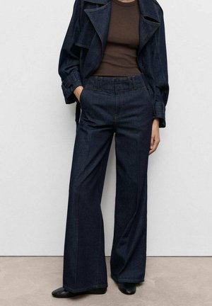 Dark denim wide-leg pants with a high waist, featuring front seams and pockets. Paired with a brown top and a dark denim jacket.