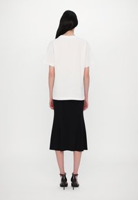 Balta kokvilnas T-krekls ar apaļu izgriezumu, kombinēts ar melnu paplatinātu svārku. Apģērbam ir gluda tekstūra un tas krīt nedaudz zem ceļgaliem.